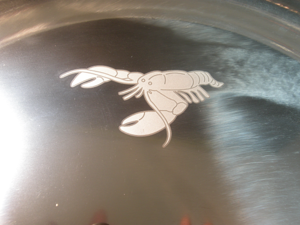 Two-tone laser marked logo on a polished stainless steel platter — deep engraved outline with white surface fill, fiber laser marking